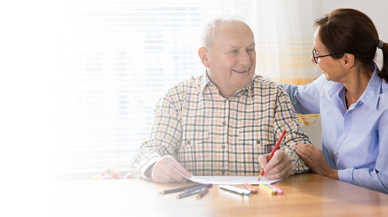 Senior man and caregiver engaged in an art activity at a memory care community.