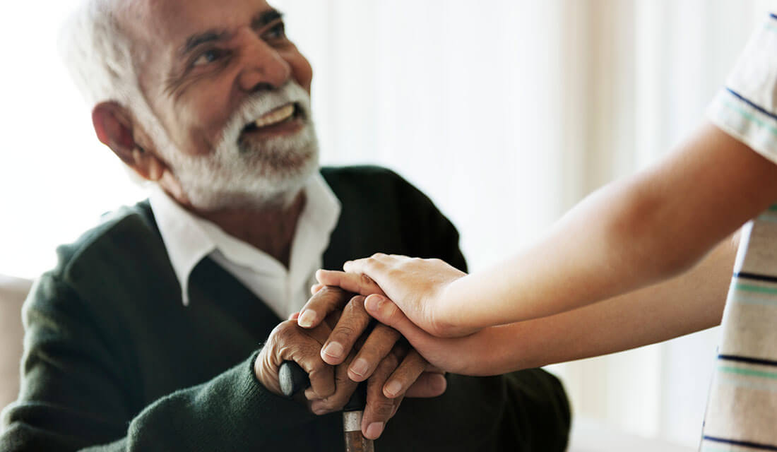 Smiling elderly man holding hands with a young person, showing a moment of connection.