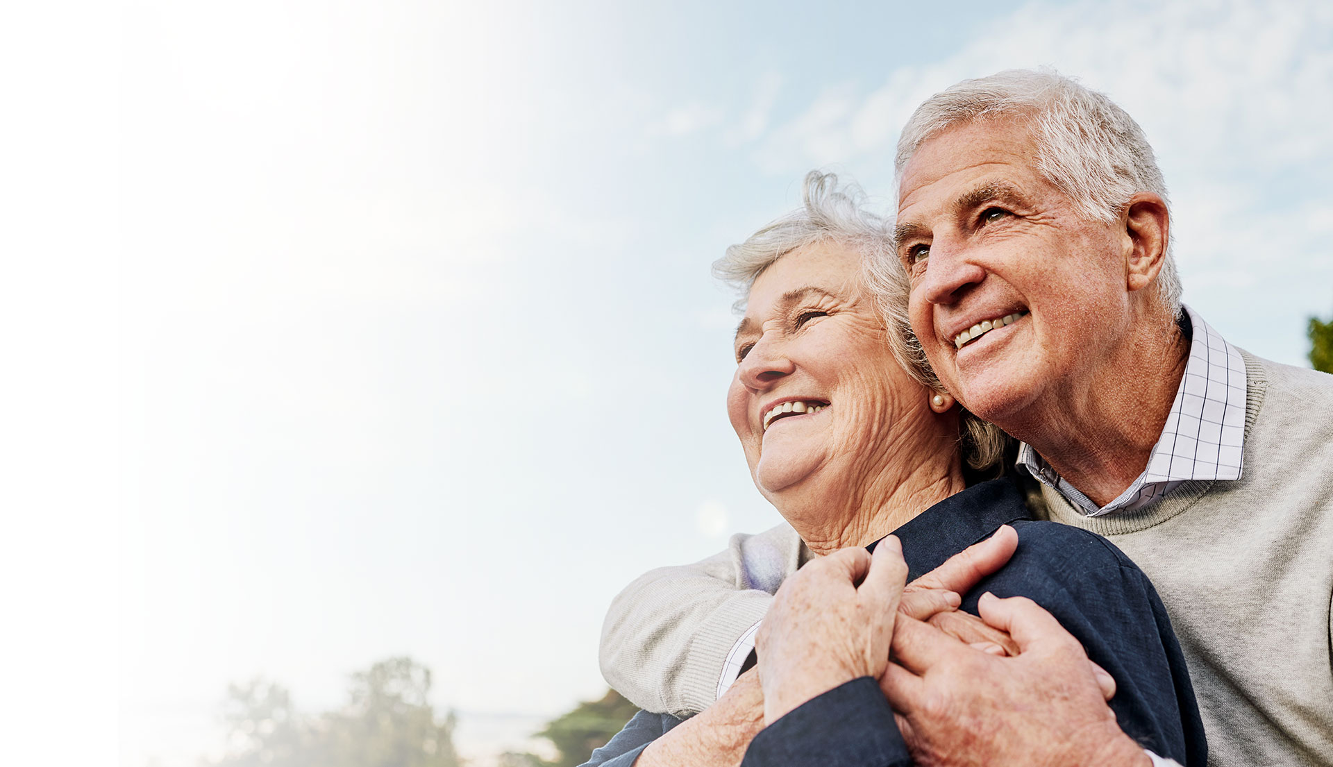 Smiling senior couple embracing outdoors at a senior living community.