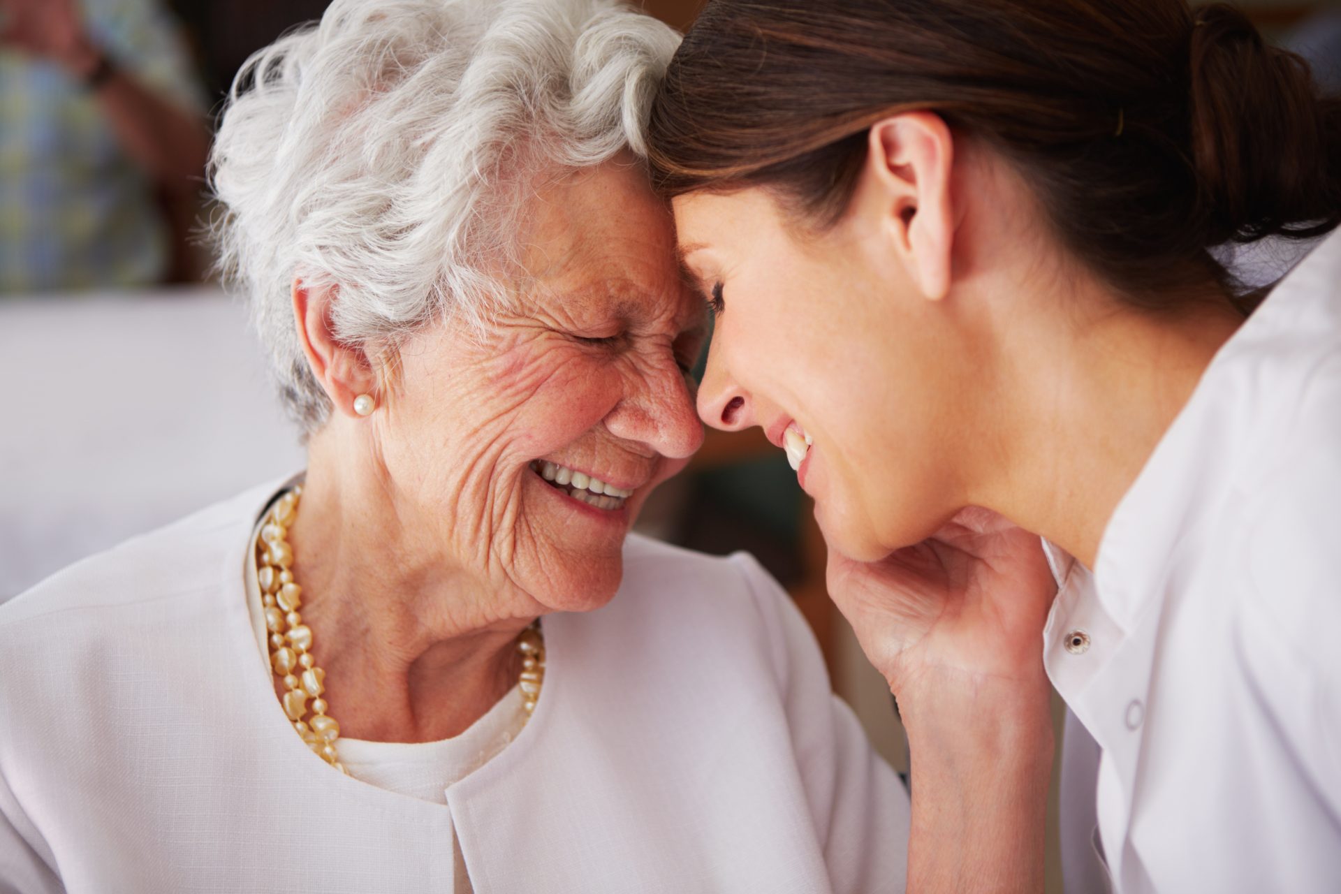Smiling elderly woman and caregiver sharing a joyful, close moment together.