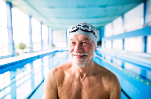 Senior man in swim cap and goggles smiling in an indoor swimming pool at a living community.