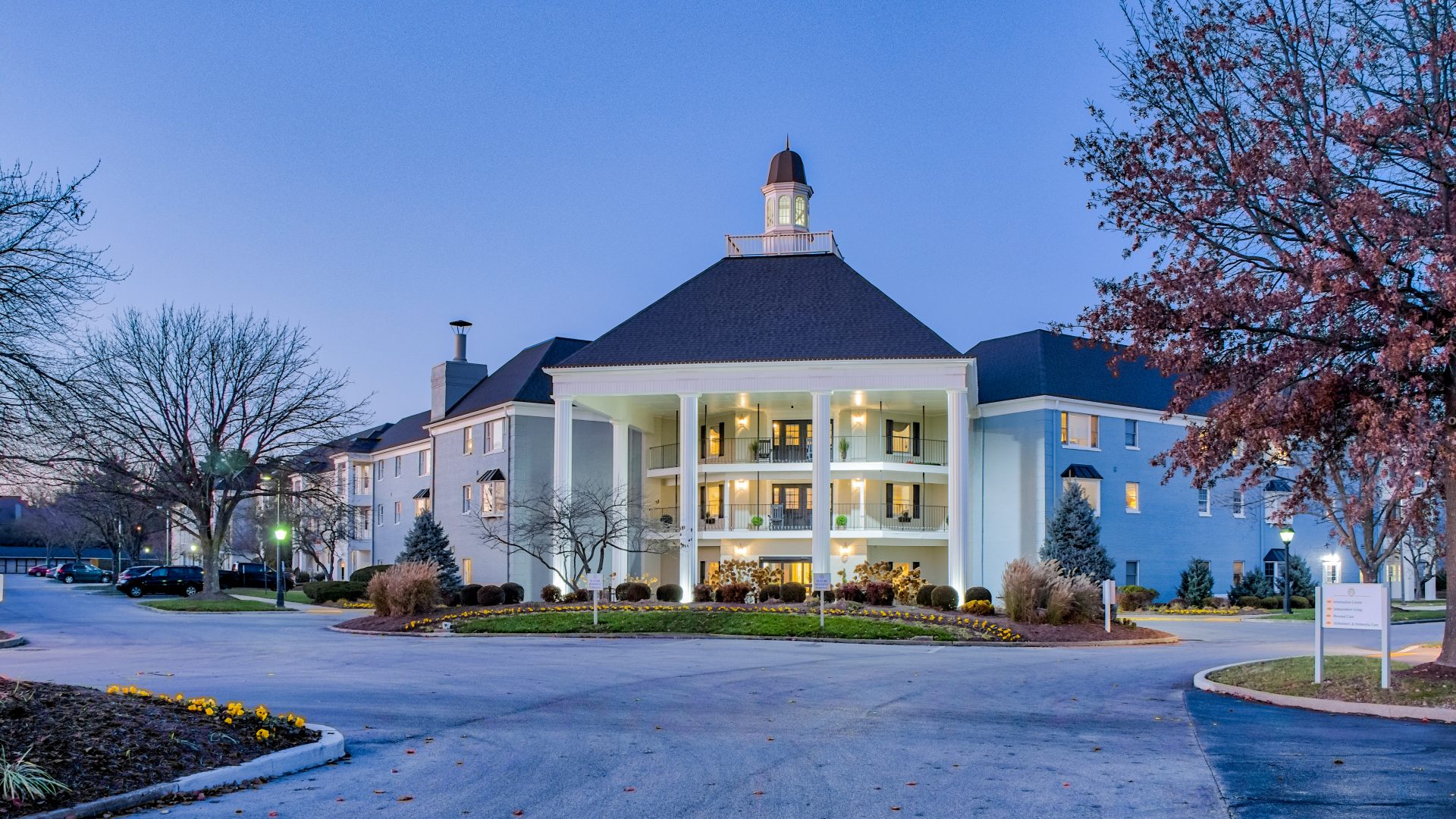 Elegant living community with grand entrance, illuminated columns, and landscaped surroundings.