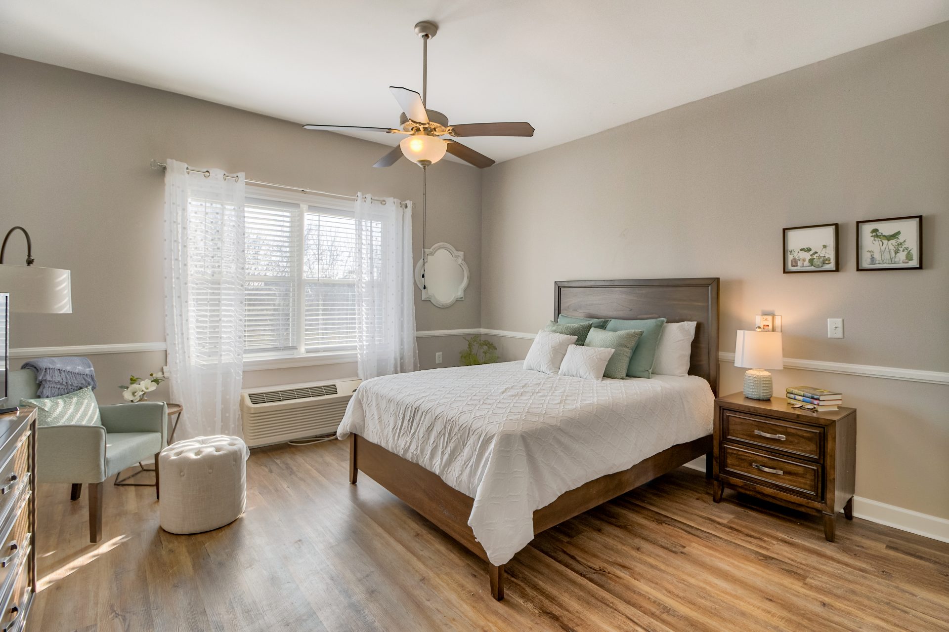 A cozy senior living unit bedroom with a large bed, bedside table, armchair, and ample natural light.