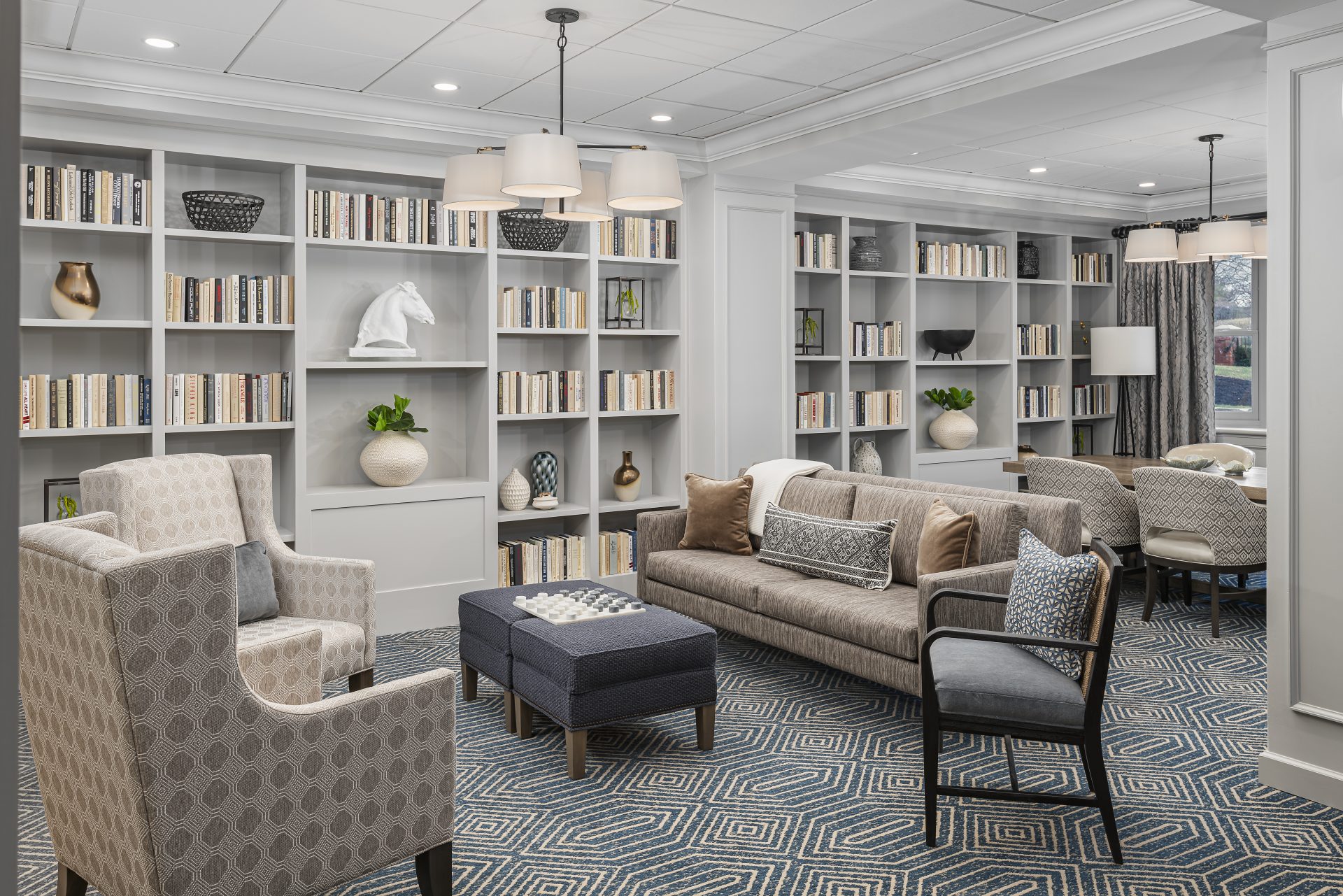 A cozy and elegant common area in a senior living community featuring bookshelves and comfortable seating.