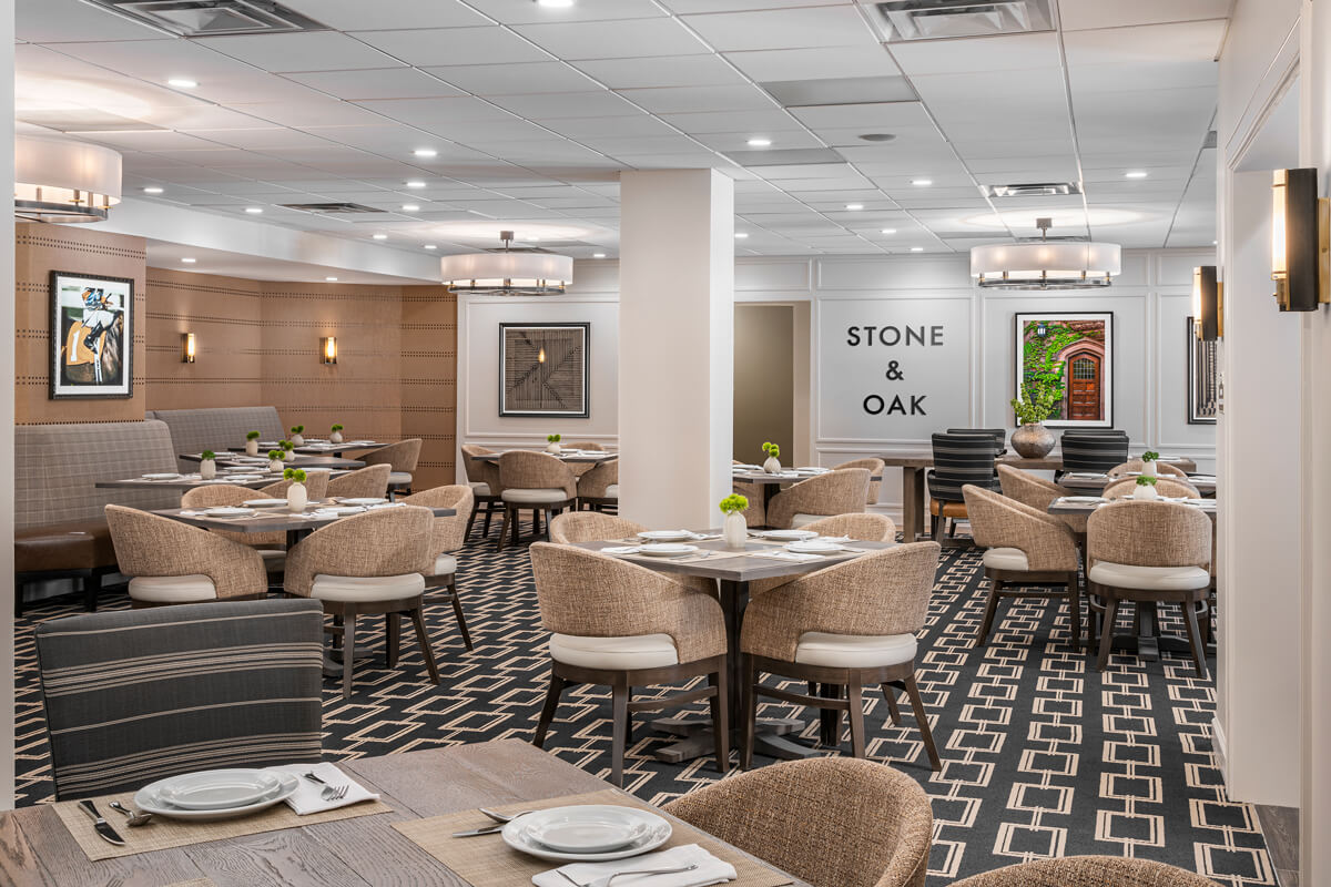Elegant dining area with beige chairs, modern decor, and Stone & Oak sign in a senior living community.