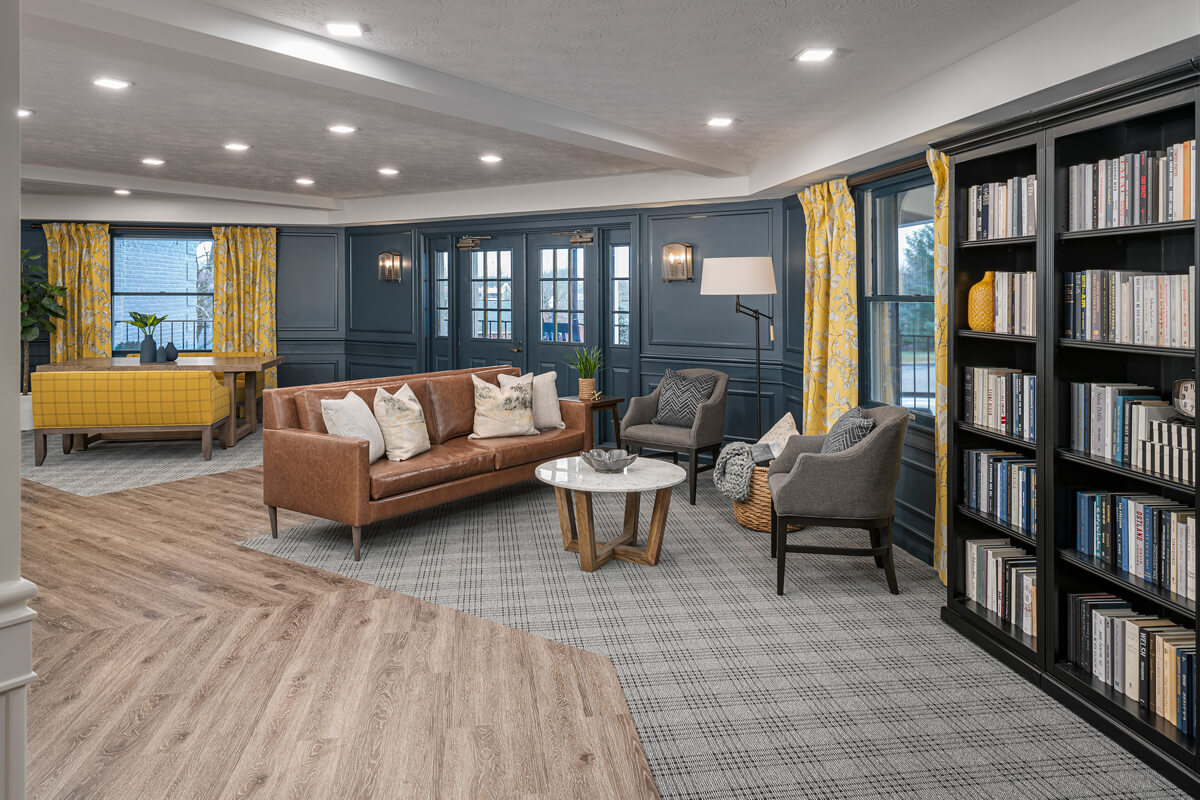 Modern living area with comfortable seating, bookshelf, and yellow curtains in senior living community.