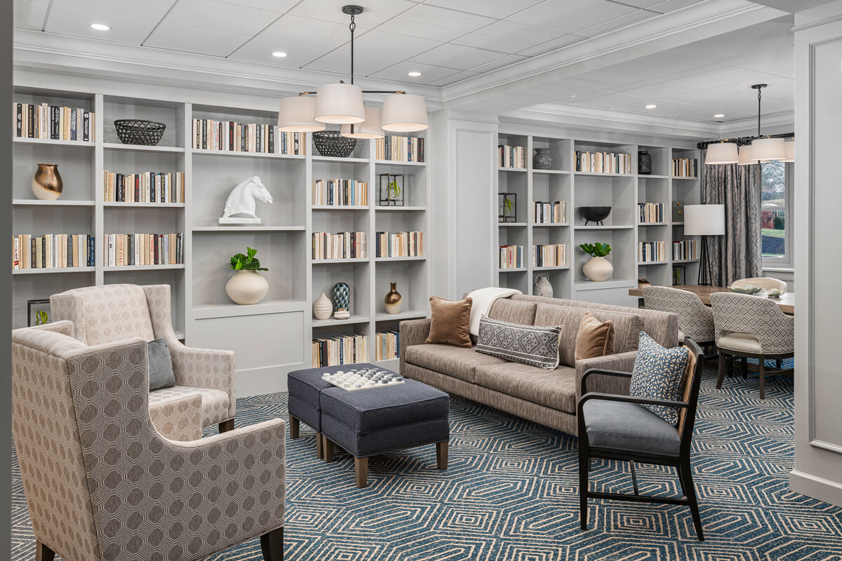 Spacious lounge area with comfortable seating and bookshelves in a senior living community.