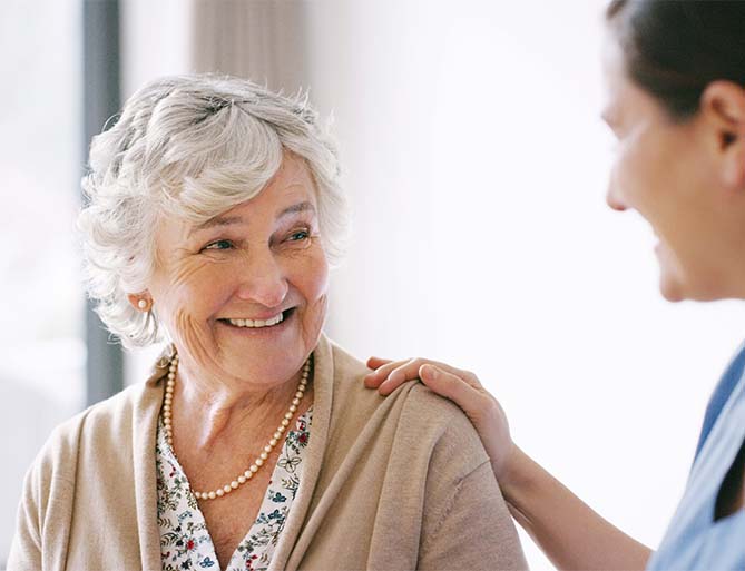 Smiling elderly woman receiving support from a caregiver at a senior living community.