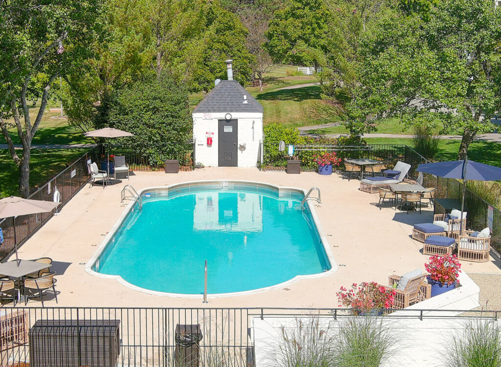Outdoor swimming pool with lounge chairs and umbrellas in a landscaped setting.