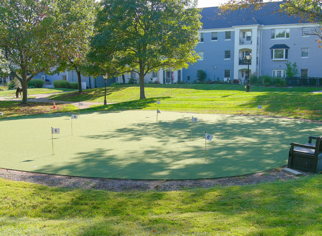 Community putting green surrounded by trees and a large residential building.