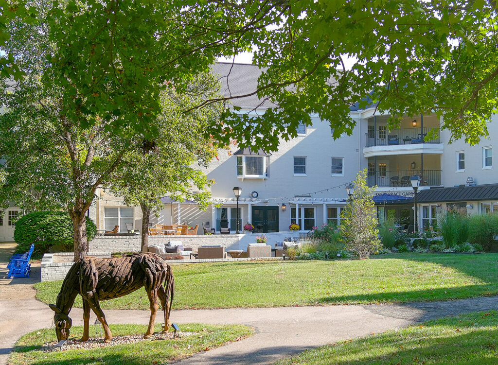 Lush garden with a metal horse sculpture in front of a multi-story building.