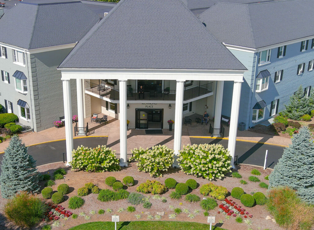 Aerial view of the main entrance to a large building with white columns and landscaped gardens.