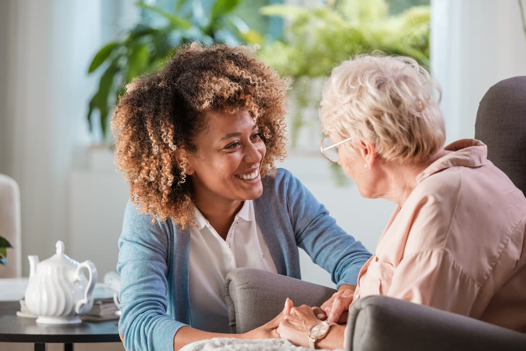 Young woman leans down to speak to seated senior woman