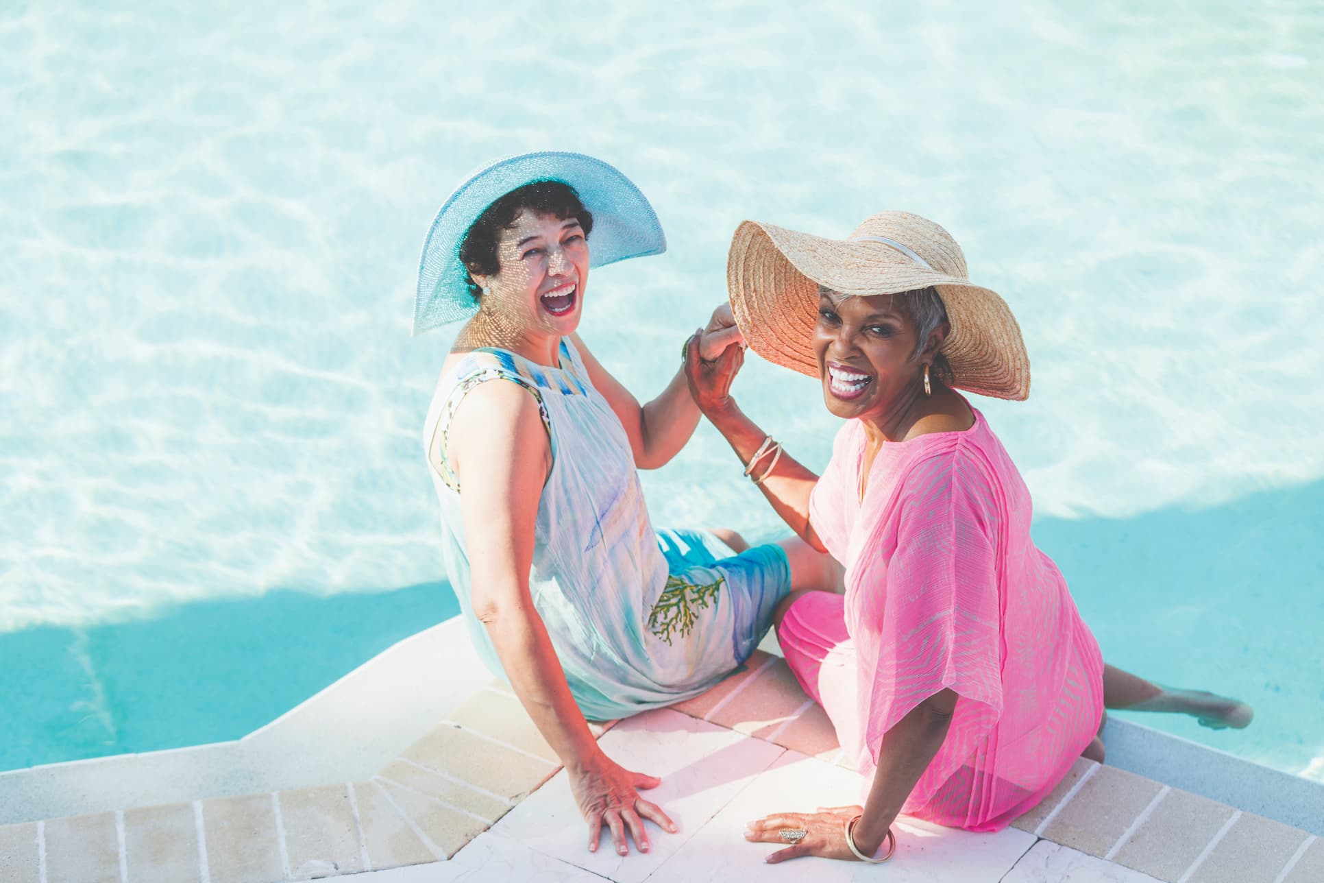 Two senior women laughing at the edge of a pool