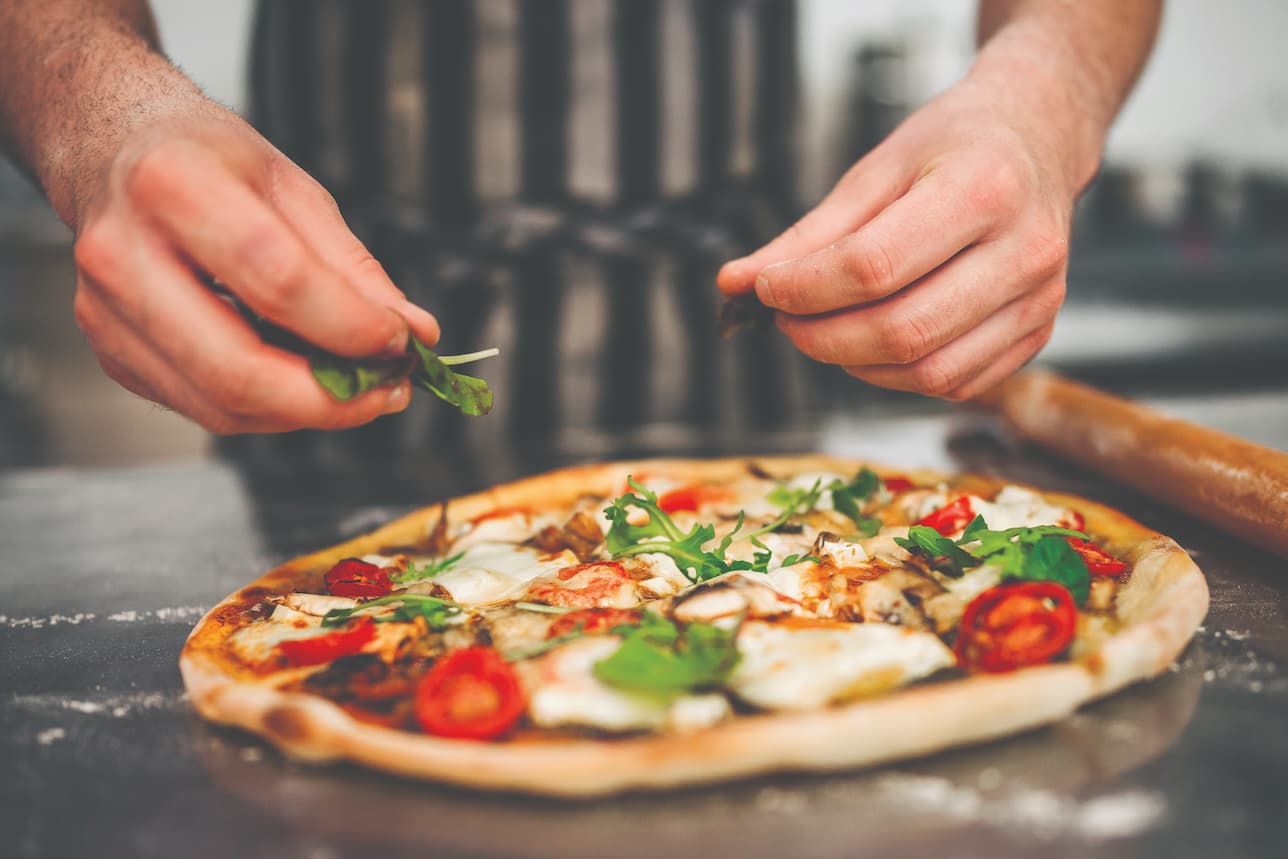 Close up of chef putting toppings on homemade pizza